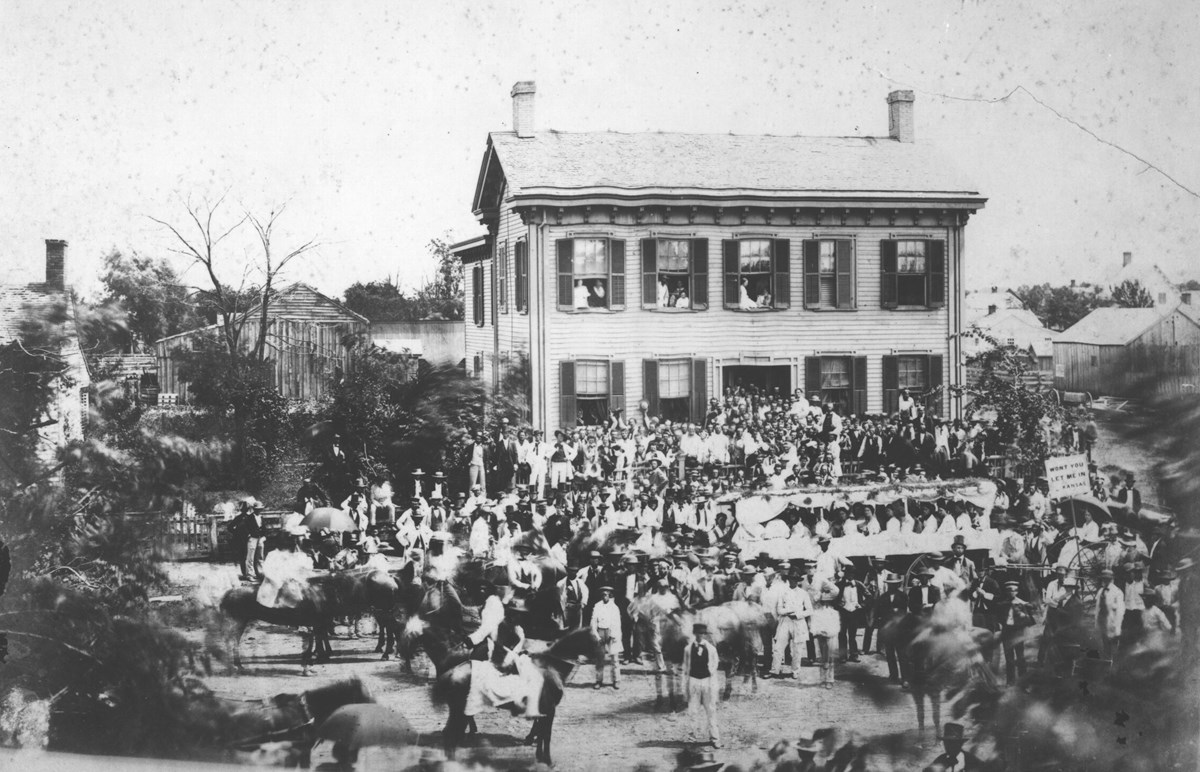 Black and white photo of Lincoln Home with a crowd of Lincoln political supporters and admirers gathered on street out front and house steps
