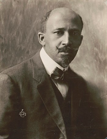 African American man in suit and bowtie, bald on top with hair on sides of head, small pointed beard/goatee, and mustache, upturned at ends