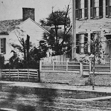 Close up of the northwest corner of the Lincoln Home, viewing from southwest. A portion of the white, one-and-a-half-story house of the neighboring northern lot of the Lincoln Home can be seen.