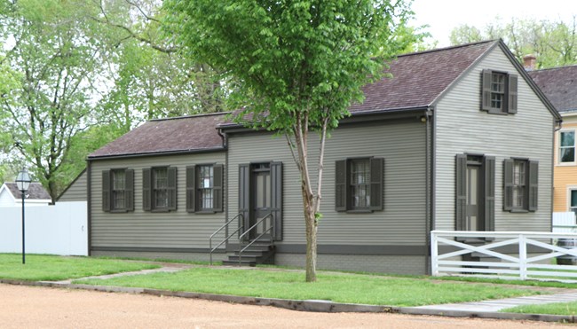 small, one-and-a-half story gray house with wood shingle roof and two main rooms.