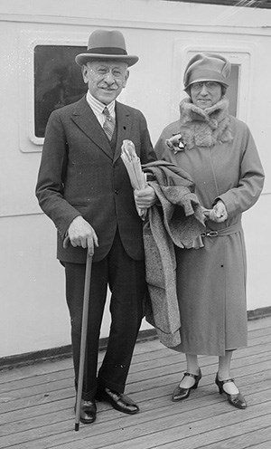 Rosenwald in suit and bat standing with a woman in a long coat, wearing hat and spectacles