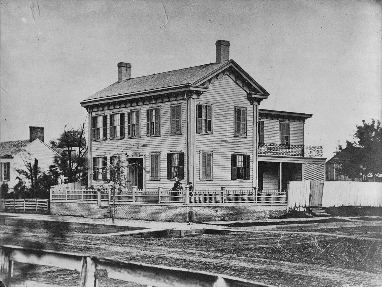 Black and White photo of the Lincoln Home, Abraham Lincoln and two youngest sons are in front yard, blurry image of a child on front walk