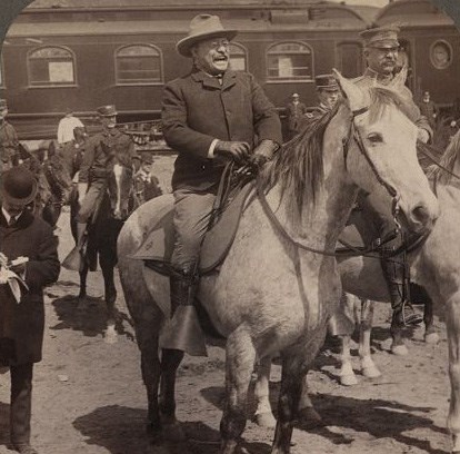 Roosevelt on a horse wearing a cowboy hat, in mid-laugh