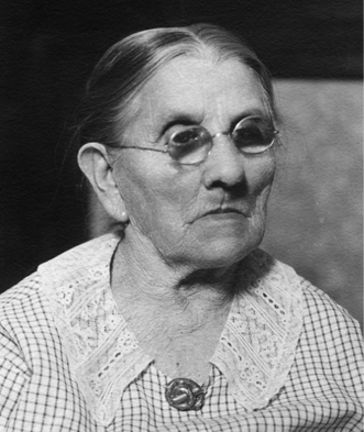 older woman with thin dark hair pinned back and round spectacles