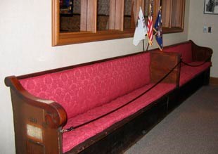 A wooden church bench and pew with red cushion