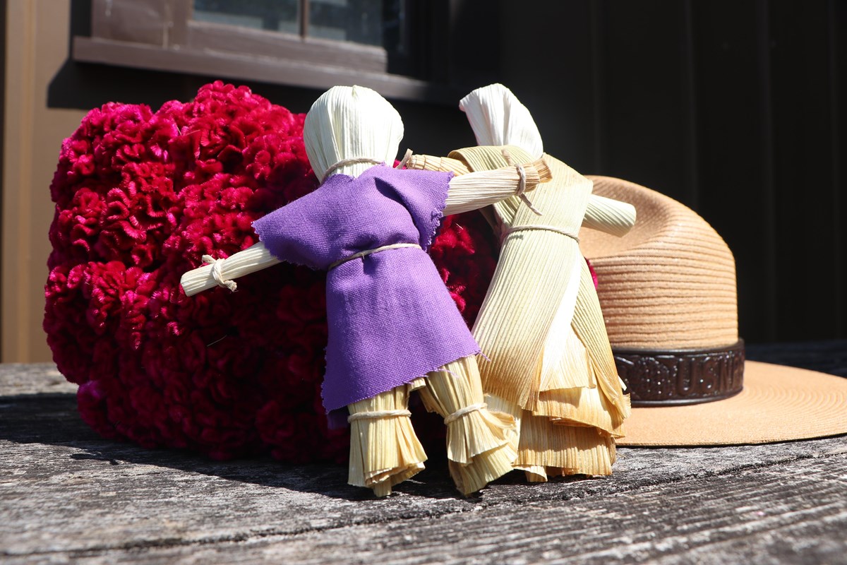 Corn Husk Dolls Corn husk dolls sit near red flowers and a tan ranger hat.