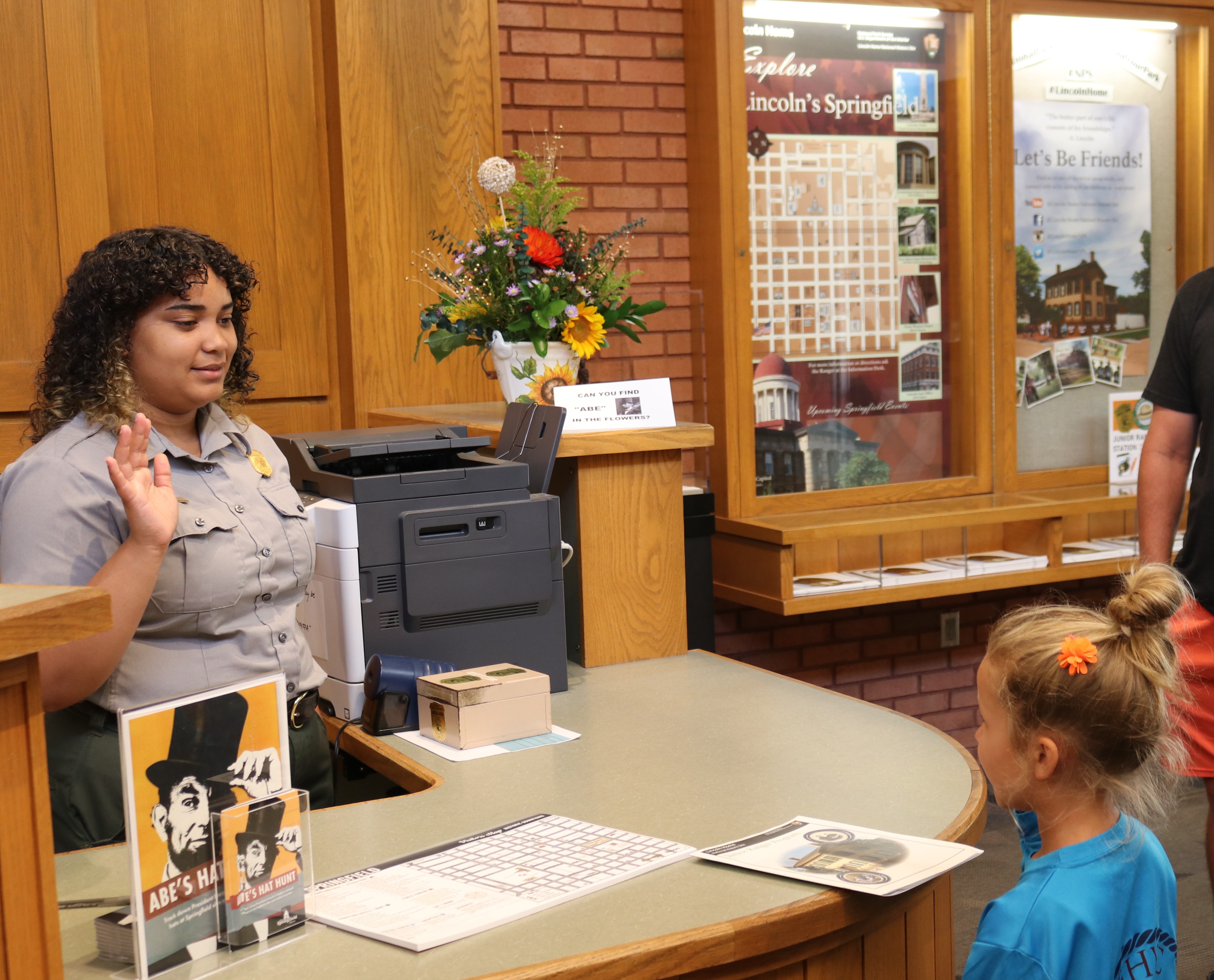 a uniformed park ranger leads a LIHO junior ranger in the junior ranger pledge at an information desk