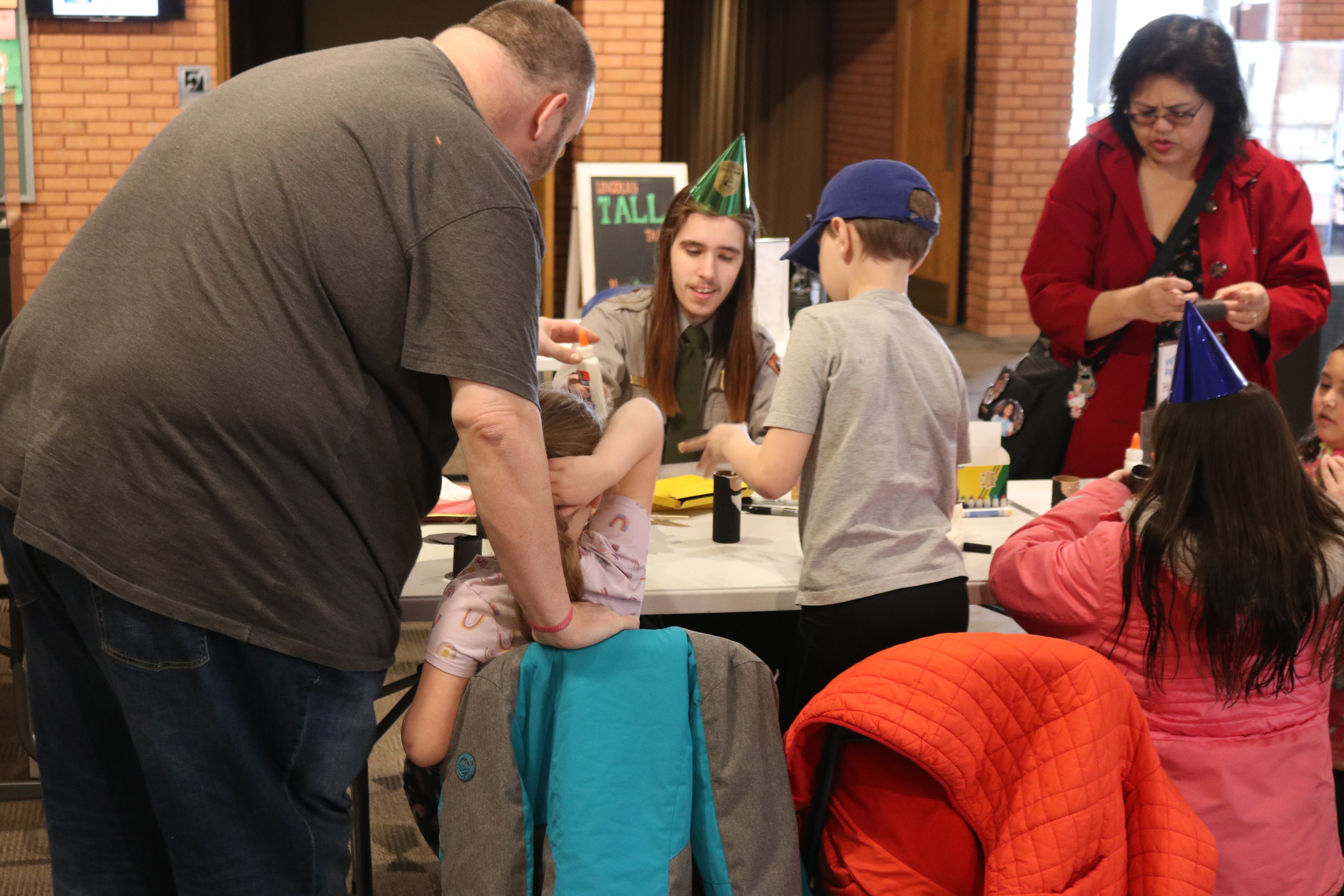 Children make crafts with a park ranger wearing a birthday hat