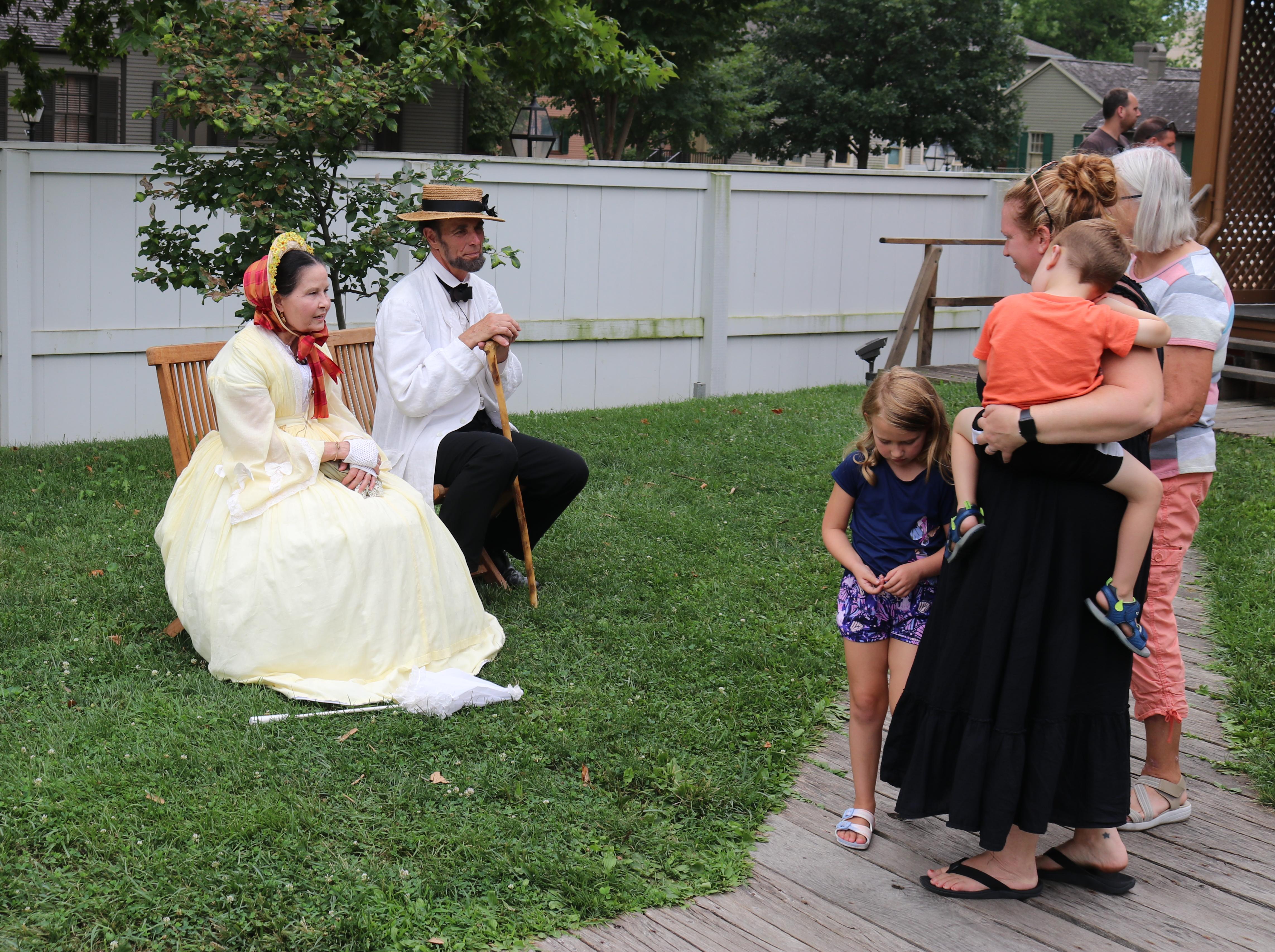 actors dressed as Abraham and Mary Lincoln sit with visitors in the Lincoln Home backyard.
