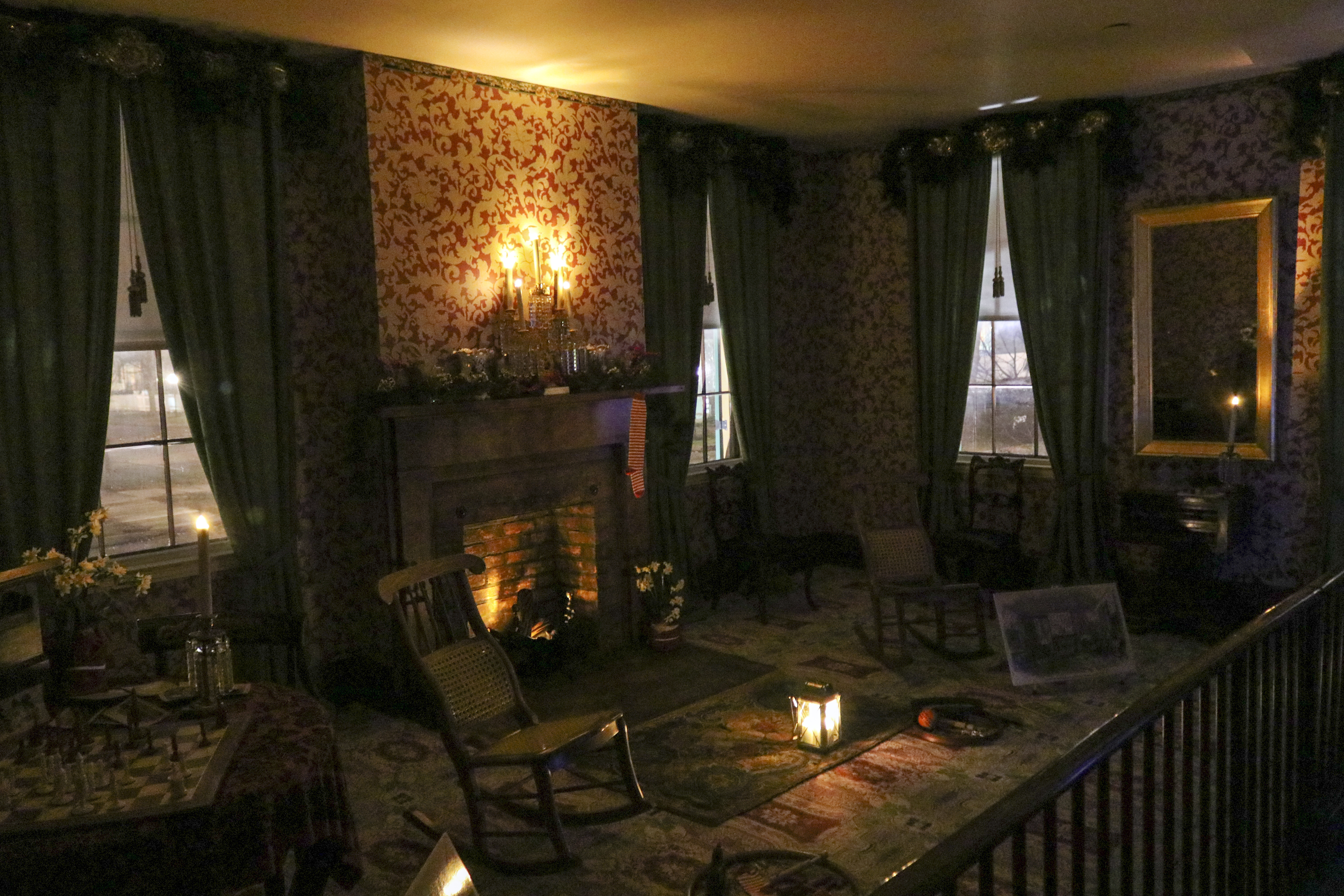 LIHO_candlelight_tours A 19th century parlor with bright red wallpaper is dimly lit by candlelight.