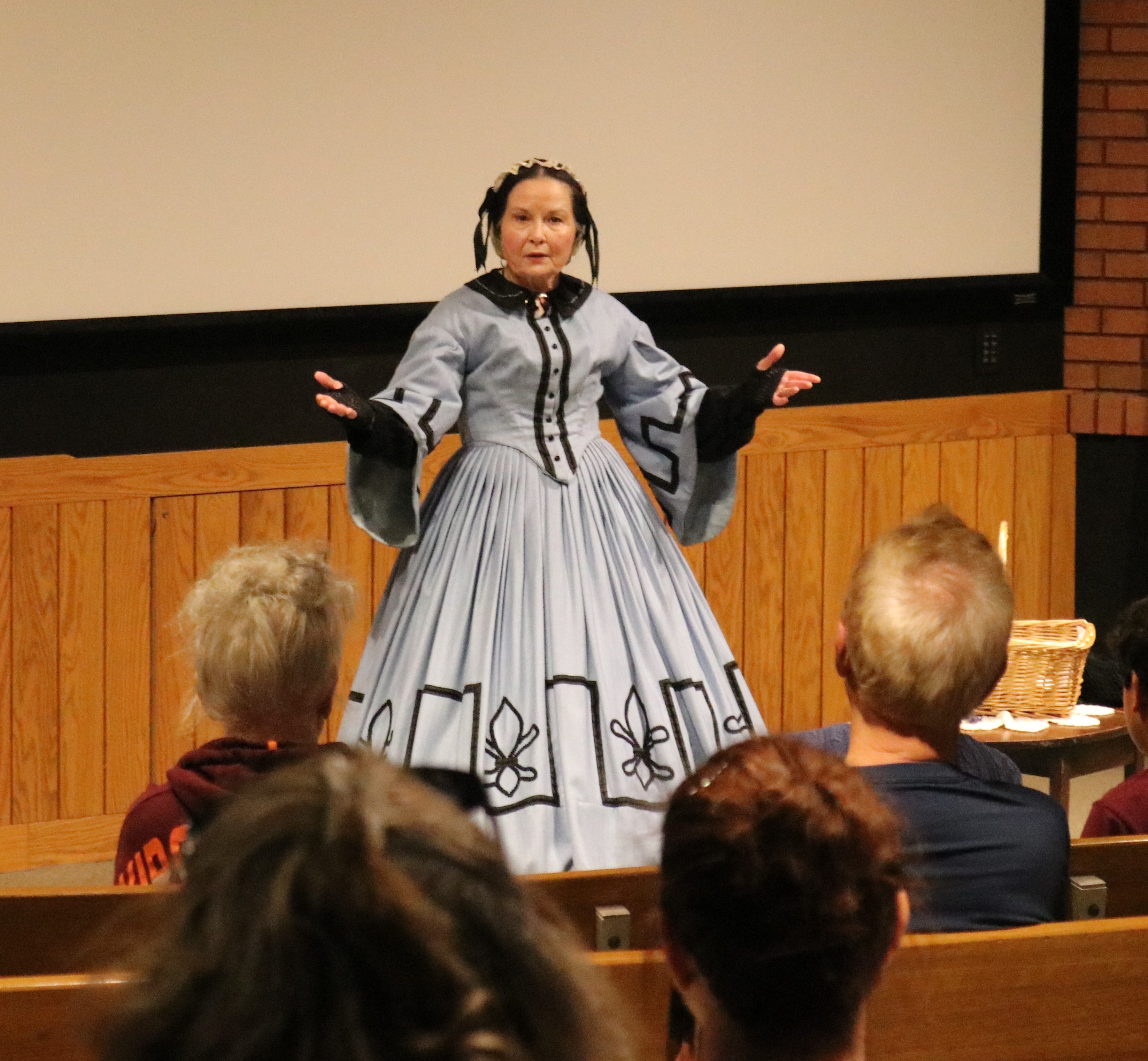 Pam_Brown_Our_Sons_03_23 An actor, wearing a blue 19th century gown, speaks to a crowd.