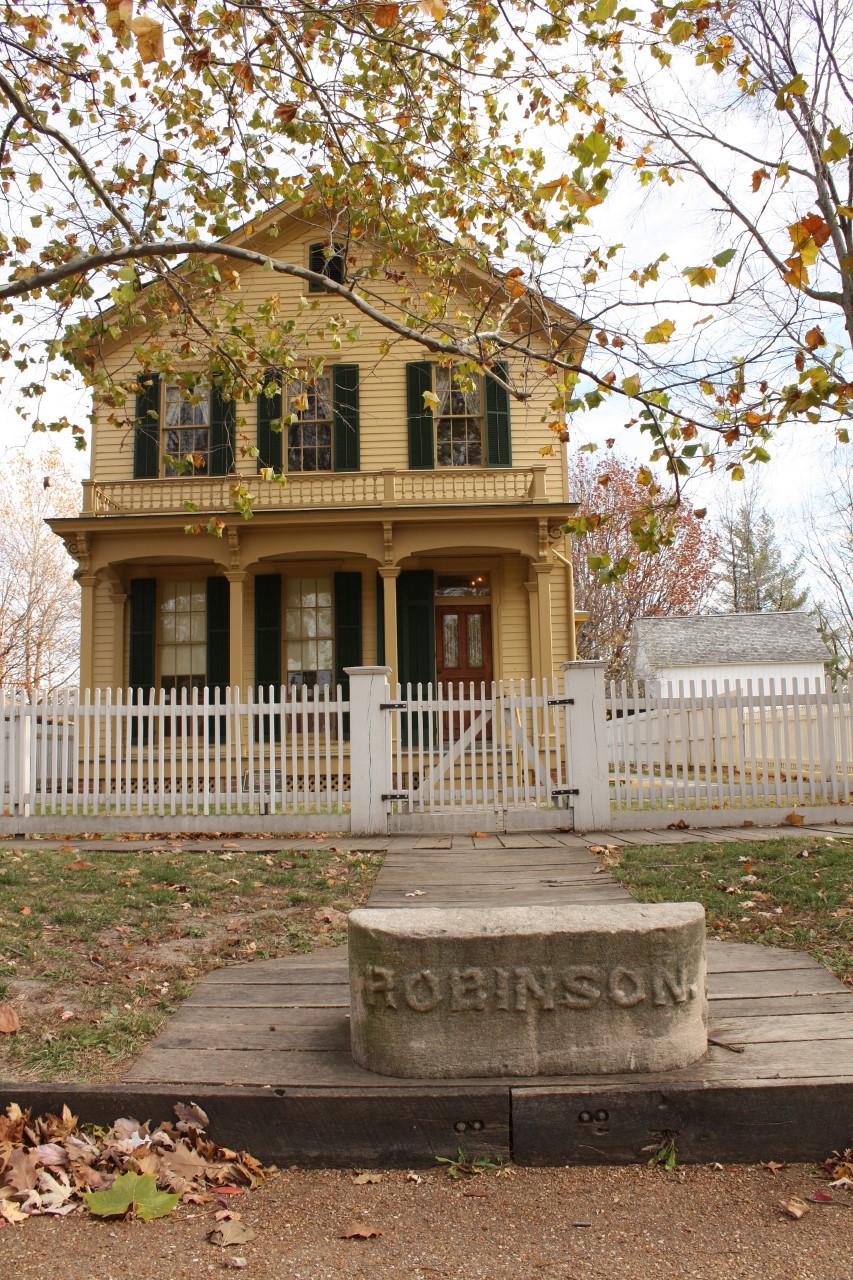 yellow 2-story house with green shutters and front porch. Stone in front of house has etched name "Robinson"