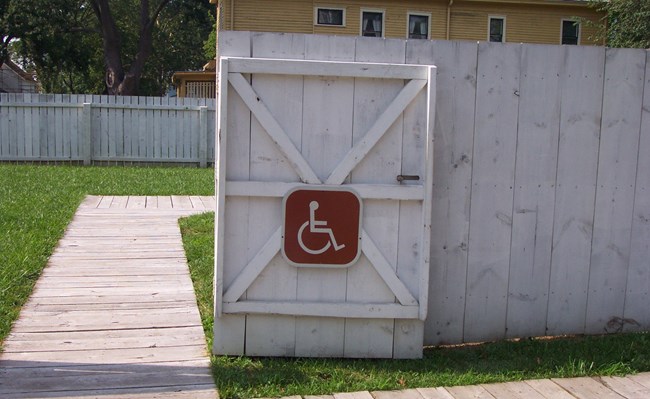 Open white wooden fence gate with wheelchair sign