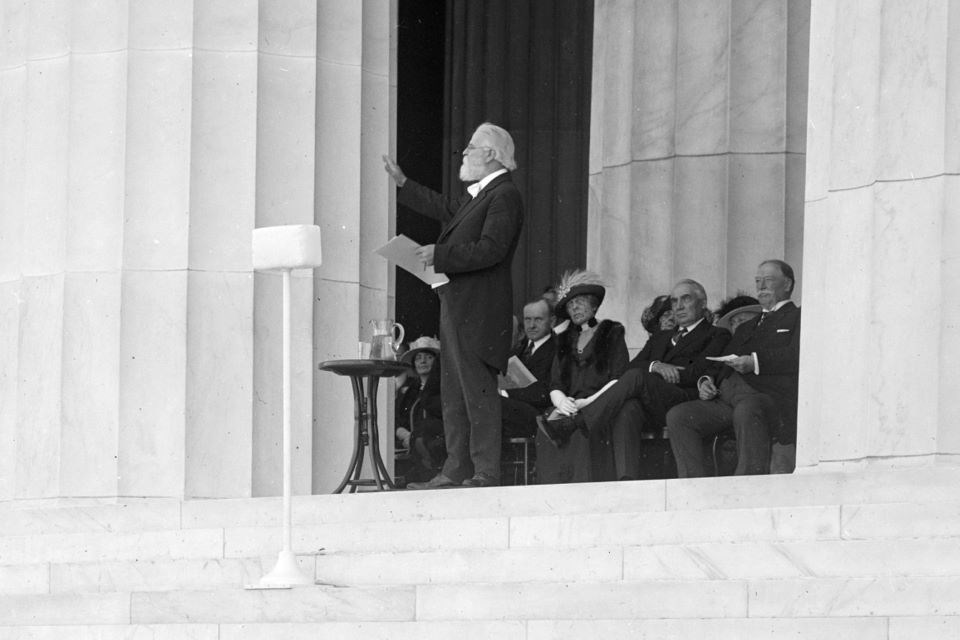 A man stands at a microphone while people seated behind him listen.