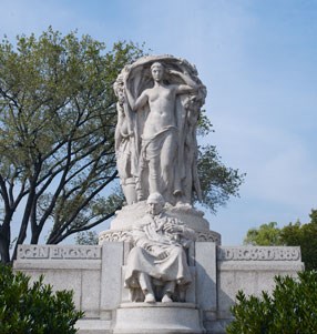 granite statue of man seated with figures support urn above