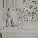 Statue of Bald Eagle against white wall with words carved in it adjacent to it