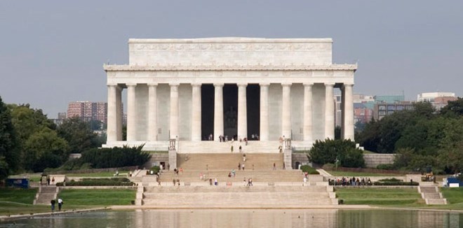 Large white building with Greek style architecture, white stairs, and reflecting pool