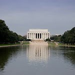 White marble building with reflection in the reflecting pool lined with green trees