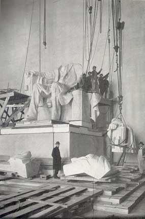 Men working on statue being assembled utilizing rope and pulley system to put pieces of it together