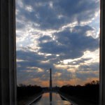 sunrise with clouds behind the washington monument in the distance, reflecting pool in the foreground. photo taken through the memorial columns.