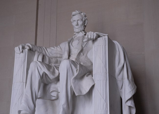 A white marble statue of President Lincoln seated in a chair.