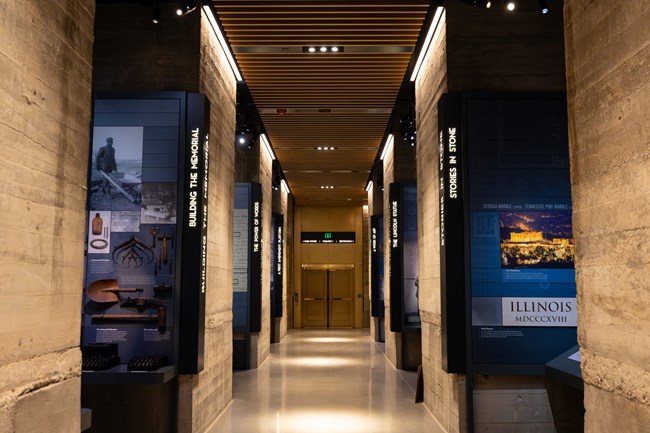 A wide hallway lined with exhibit spaces with photos, text, and artifacts.