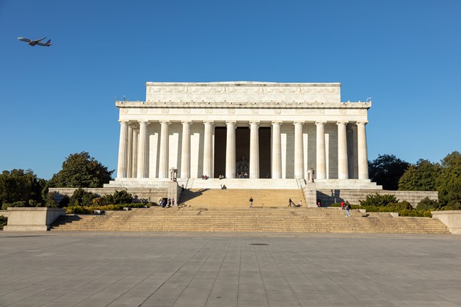 A series of wide steps lead up to a white marble rectangular memorial lined with pillars and with a statue of President Lincoln inside.