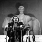Marian Anderson standing in front of microphones with Abraham Lincoln statue in the background.