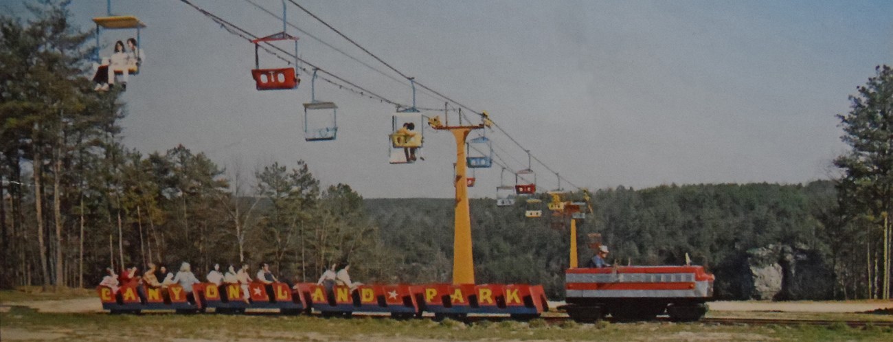 Close up of a postcard showing a chairlift going into the canyon and a miniature train pulling visitors in the foreground.