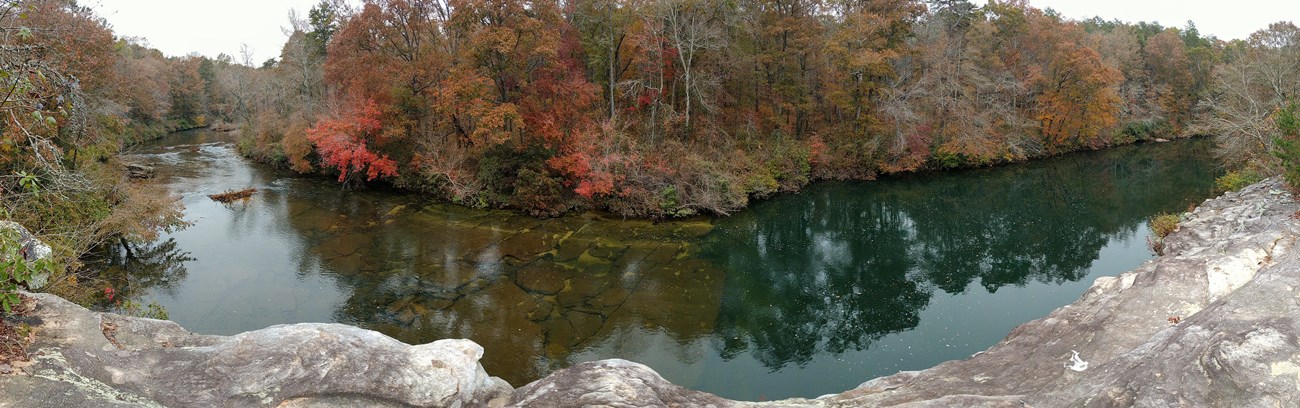A bend in the river, the banks covered with trees in fall colors,  as seen from a high rock.