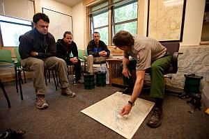 a park ranger points to a map in front of three men