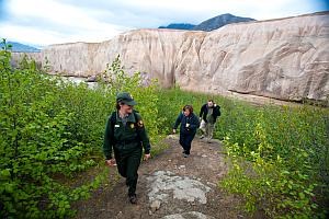 a park ranger leads two visitors up a trail