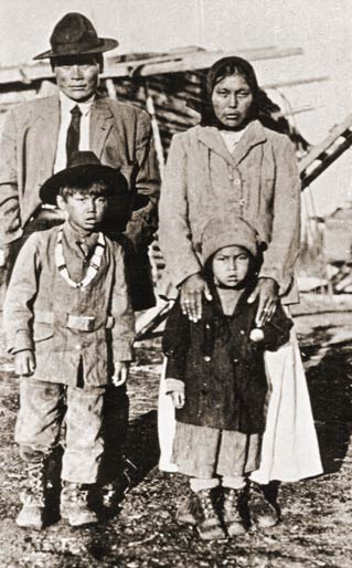 An adult couple, male and female, stand behind two male and female children, all in formal dress.