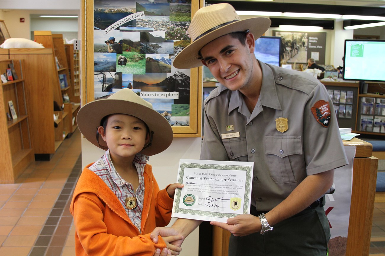 A ranger presents a child with a Jr Ranger certificate and badge