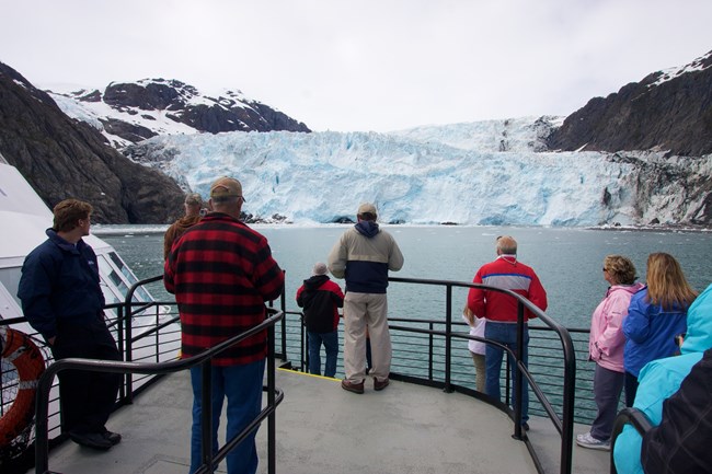 People stand on the deck of a boat looking at a glacier in front of them