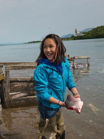 a young girl holds a piece of fish as part of traditional subsistence practices