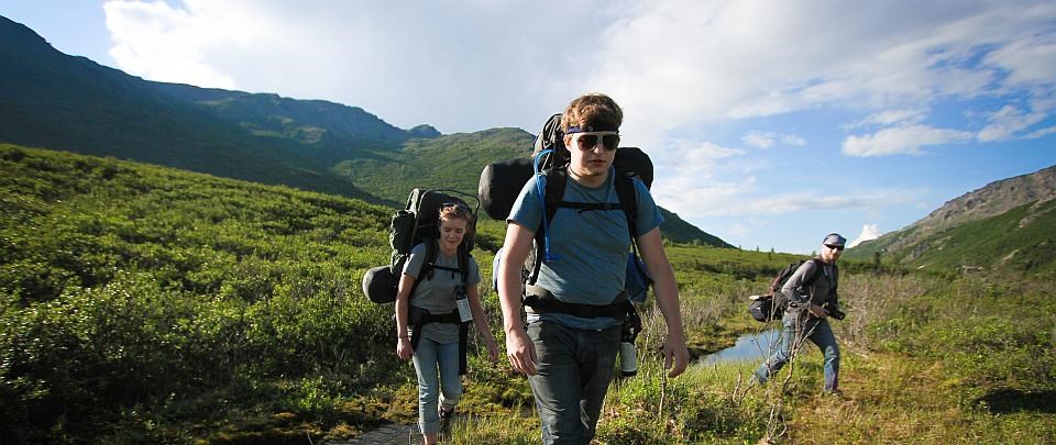 three hikers walk with packs through Denali National Park