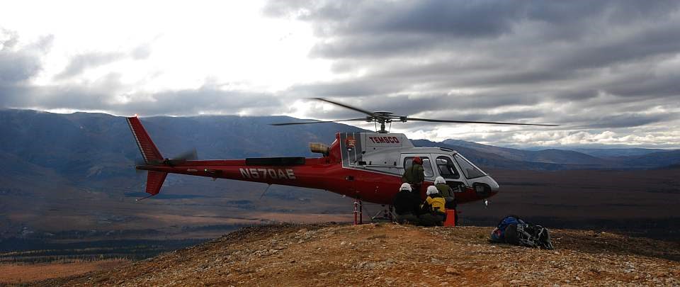 a crew wearing hardhats loads a helicopter on a hill