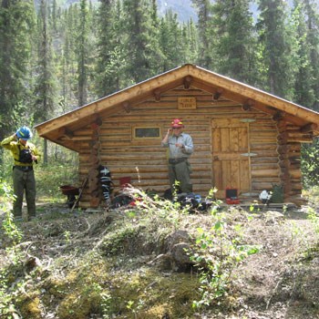 Two wildland crew members work to clear fire fuels from around a cabin. Two wildland crew members work to clear fire fuels from around a cabin.