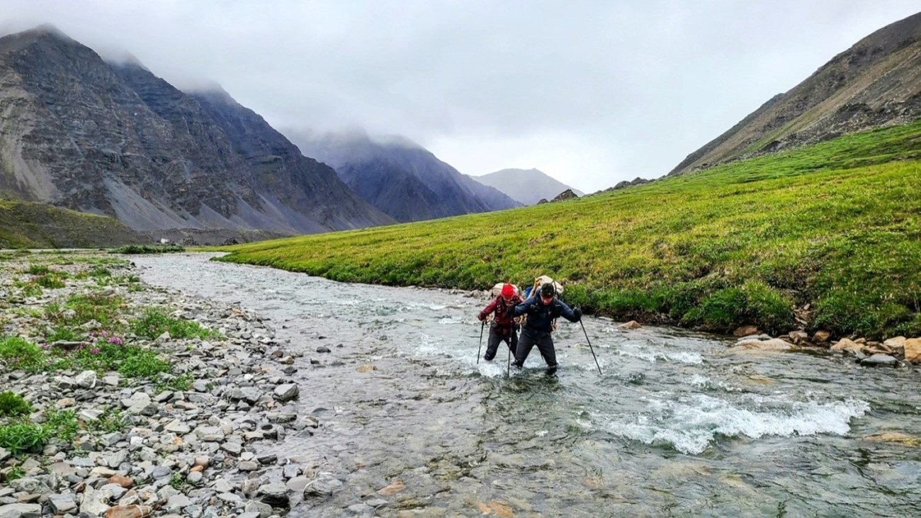 Two backpackers cross a creek in the mountains