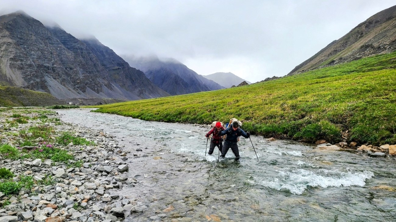 Two backpackers cross a creek in the mountains Two backpackers cross a creek in the mountains