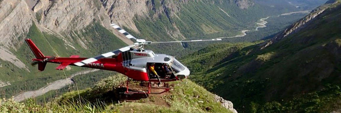 The red and white 970TH helicopter sits momentarily idle on an outcropping overlooking a valley.