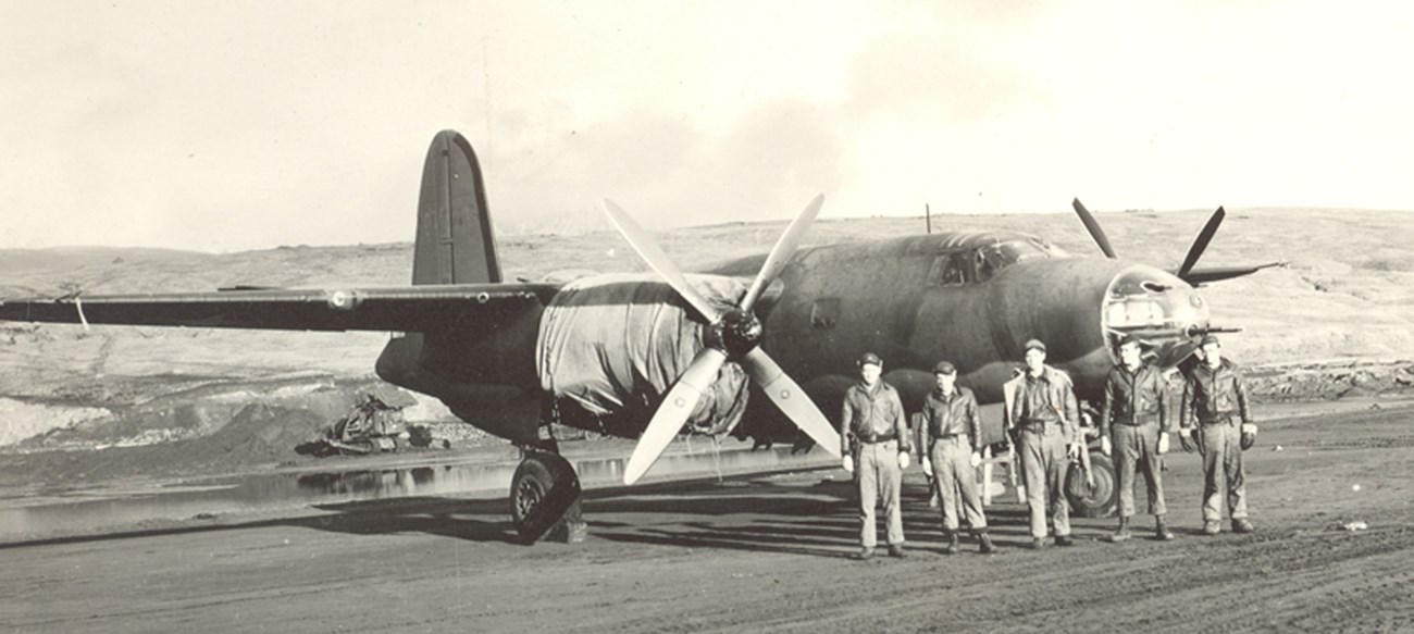 a flight crew stands in front of a propeller plane in 1942