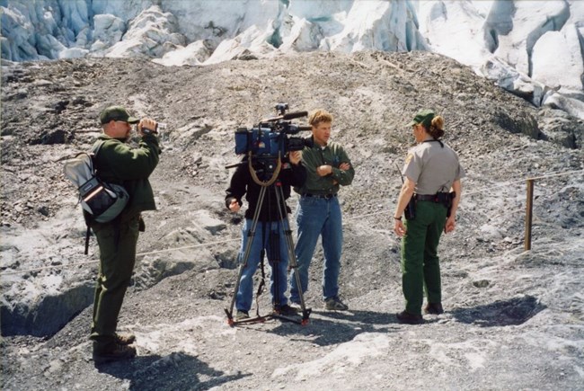 a park employee is interviewed by a news crew in front of exit glacier