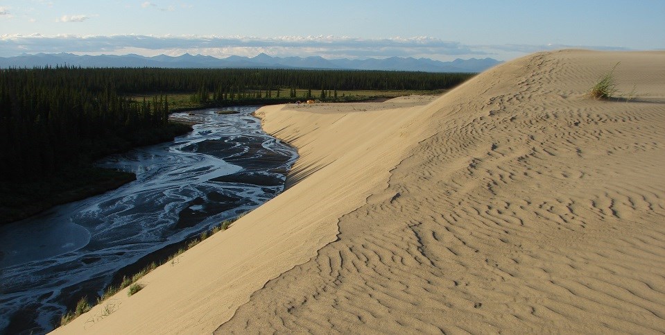 Sand dunes display wind ripples and overlook a river valley.