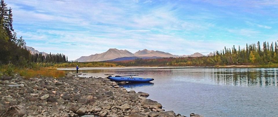 a kayak and person stop at the edge of a river in front of mountains