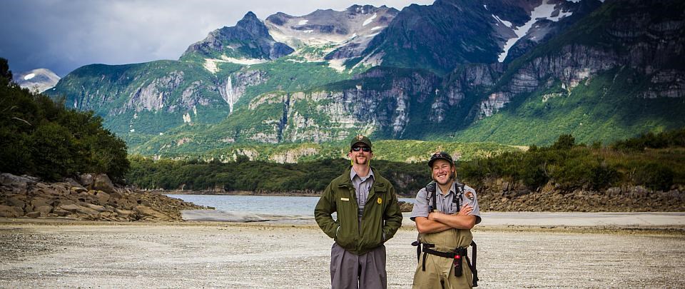 two rangers smile with in front of mountains