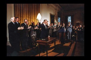 A group of lawmakers stand in a room clapping. President Carter is near the center.