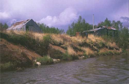 Mary's Camp along the Alagnak River. Photo courtesy of Janet Curran, USGS. Two metal structures sitting on the bank of a river.