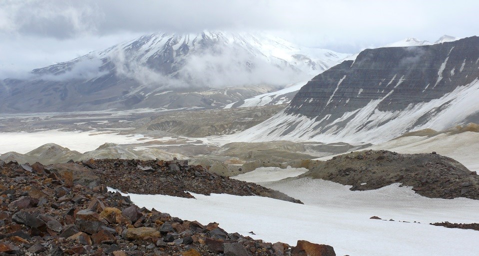 Red rocks and a glacier are backdropped by snowy mountains